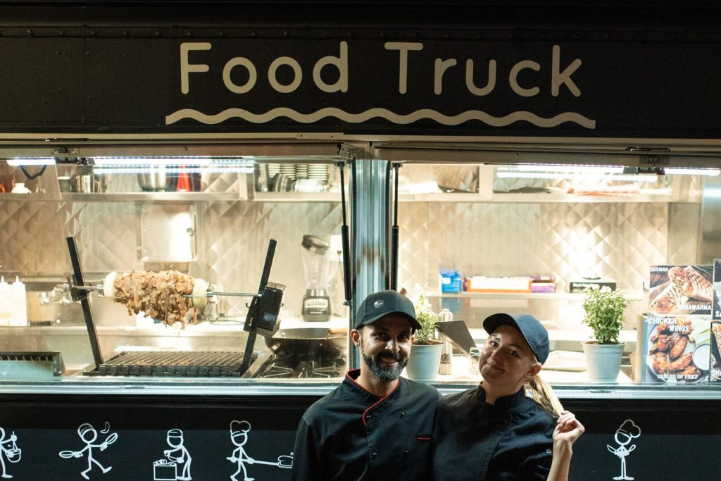 the counter of a food truck with two of the serving staff standing outside in front of the counter smiling