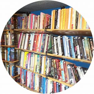 Mobile library shelving within a bus conversion. The photo shows timber shelving with library books and a book spinner alongside.
