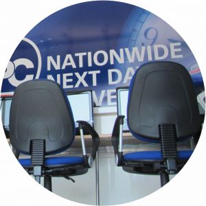 This photo of a double deck bus conversion is a close up shot of the backs of two office chairs situated in front of two computer screens. There is a promotional poster covering the windows.