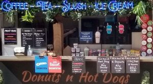 A traditional fare for a street food van. This shows a counter with price boards for a variety of drinks and biscuits and dounuts.