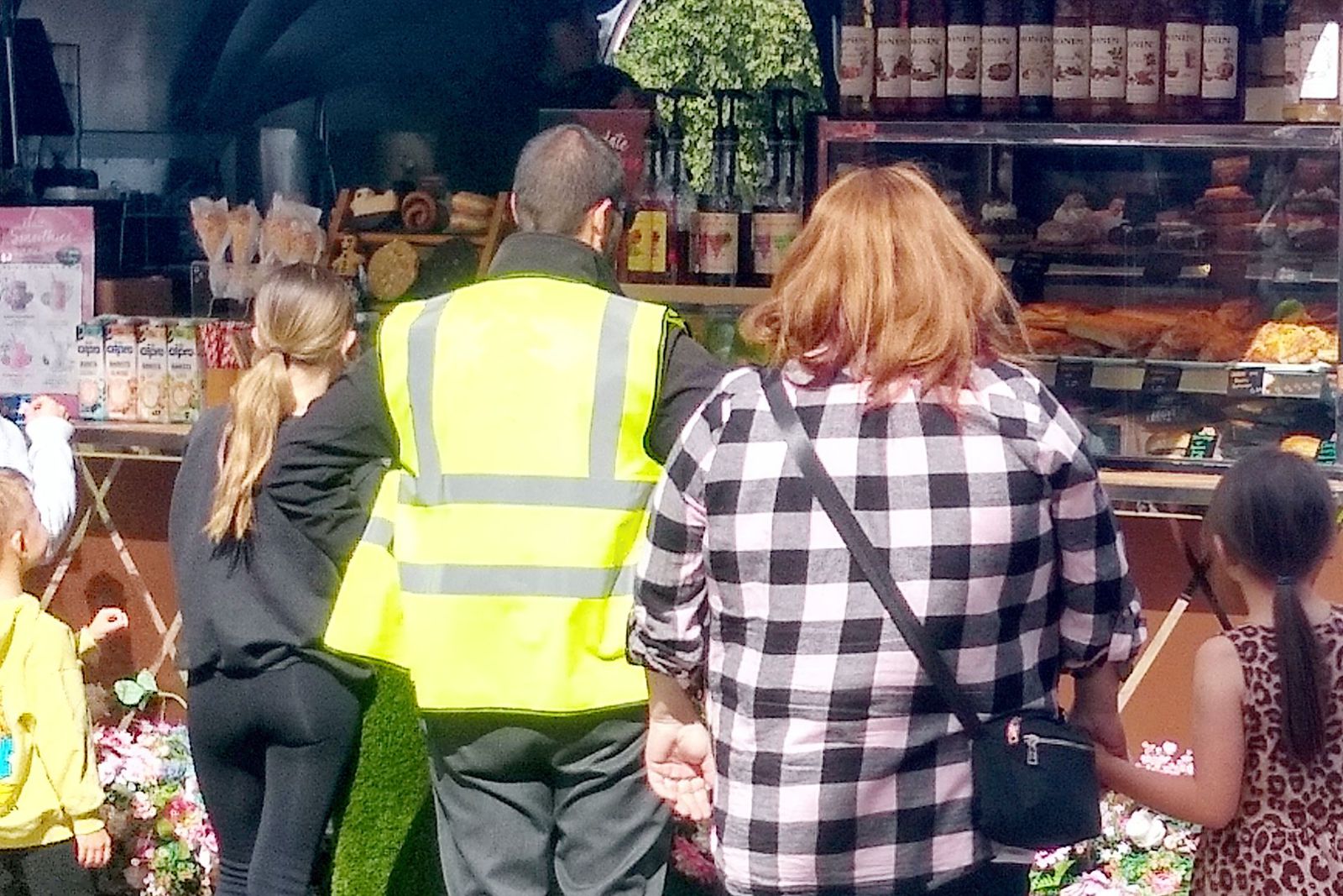 The counter with customers of a street food van selling hot drinks and heated foods including pasties and sausage rolls.