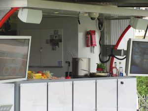 A street food van which features the counter as sliding out slightly into the crowd so that customers have a better access and view of the food on offer. There are two TV screens and these are linked to a camera to give a view of the food in preparation.
