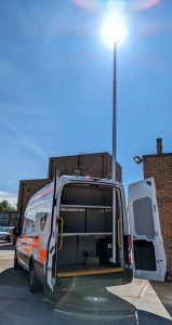 The rear of a panel van with doors open and a large mast erected with a light at the top to illuminate the ground