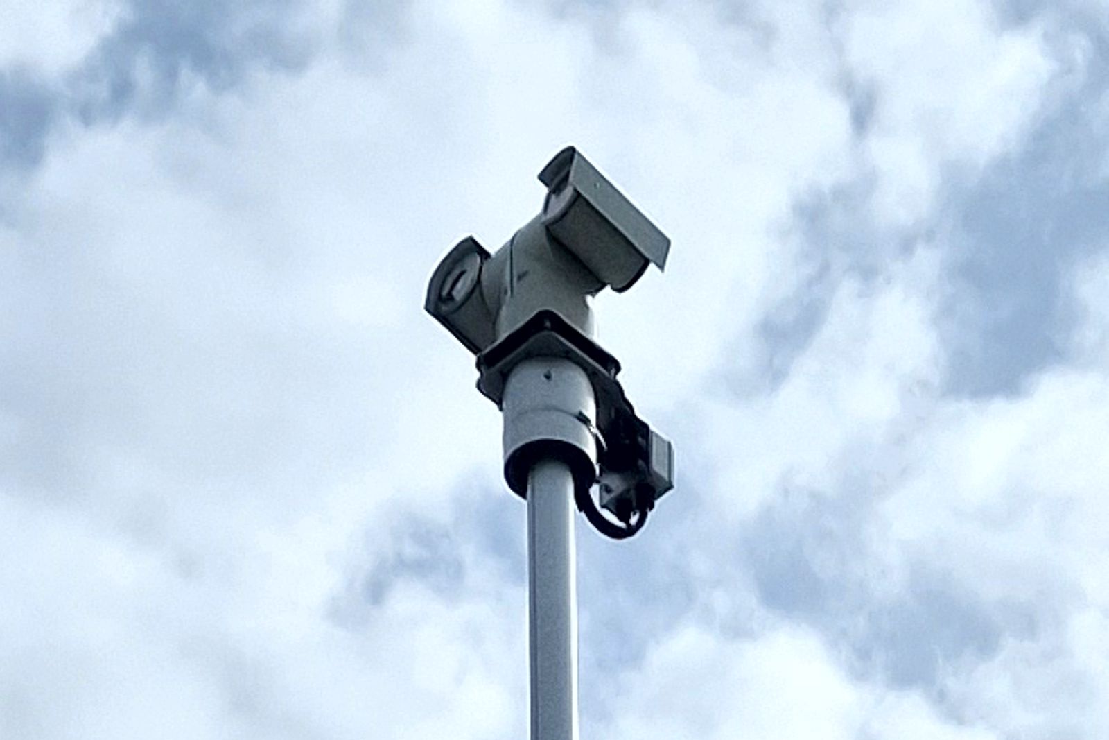 A photo of a camera mounted on a mast with blue sky and clouds in the background.