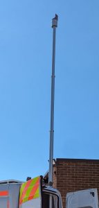A close up rear vire of a van with mast extended against a clear blue sky