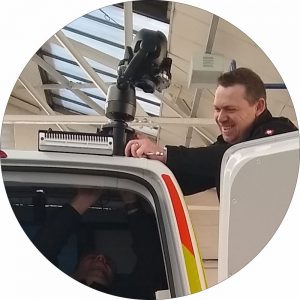A close up shot of a camera being mounted to the mast of a van in the MVTech factory. One smilling person is securing the camera with a spanner.