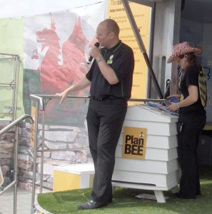 Photo of a compere with microphone in hand standing on the stage of an exhibition trailer at the Royal Welsh Show