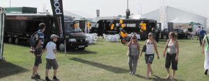 People walking past two converted single deck buses at a country show. In this instance it is the Royal Norfolk show. The buses are converted into a catering training vehicle and the other an IT training vehicle