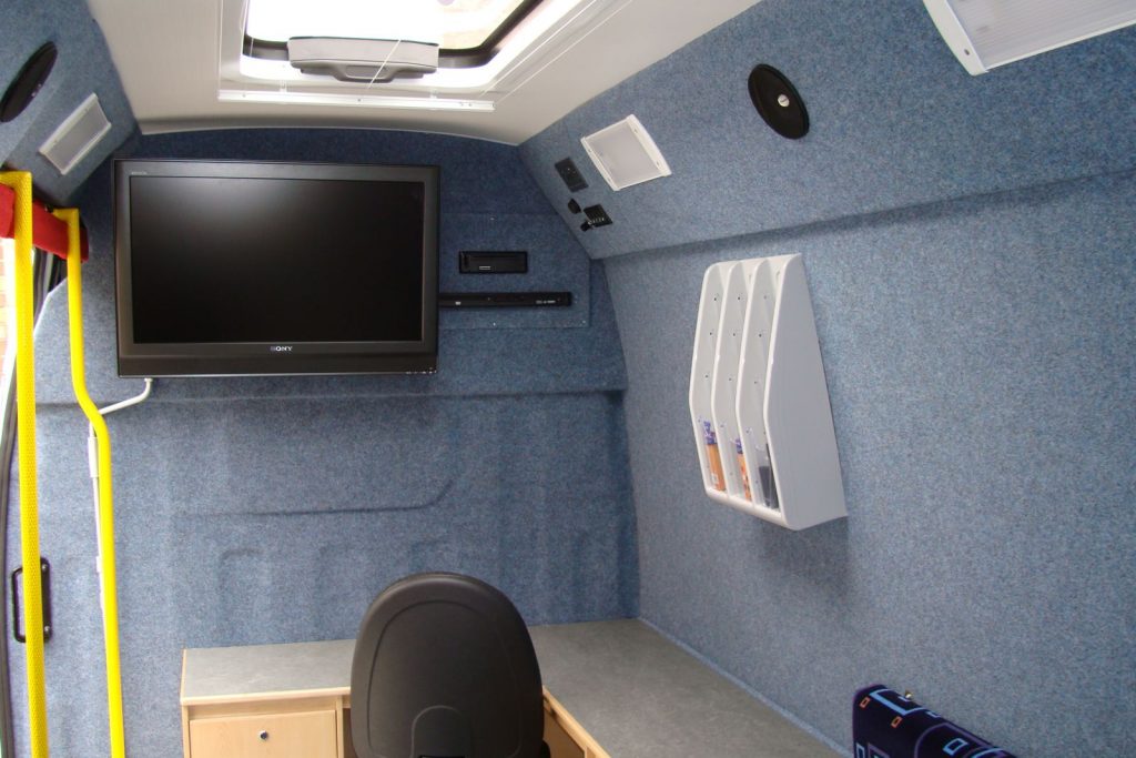 Interior view of a mobile office with all walls covered with carpet van lining in a light blue grey colour.