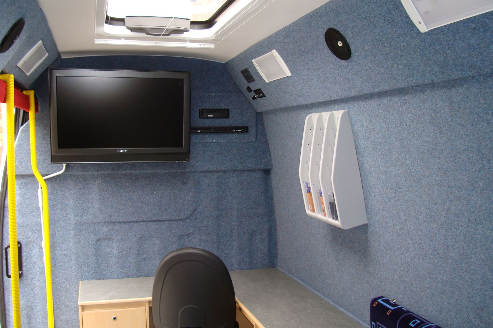 Interior view of a mobile office with all walls covered with carpet van lining in a light blue grey colour.