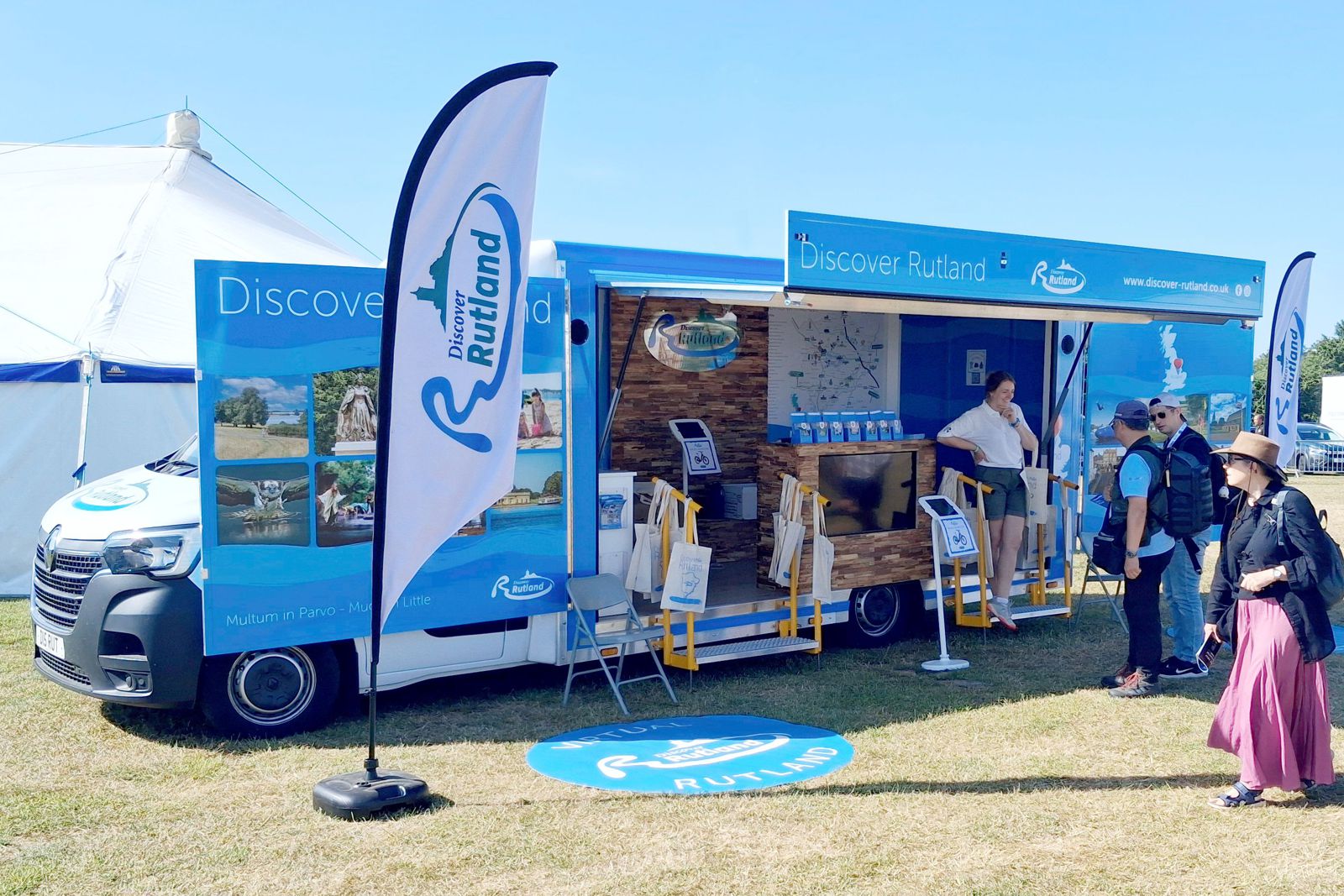 A roadshow vehicle painted in blue and covered with photos of rutland to promote rutland tourism People can be seen viewing the photo display.