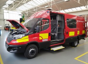 A fire services van conversion during the build process. It is painted brioght red with yellow squares and shows the side door open to reveal extra seating and storage shelves. This is typical of many emergency response vehicles used by fire services nationwide.