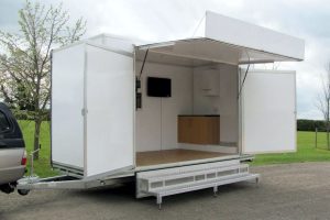 One of our used exhibition trailers, which is currently for sale. This is 4 metres long and features a hinge-up canopy with a banner board. Two large swing out display panels appear either side of the open entrance. Aluminium steps provide access to the trailer.