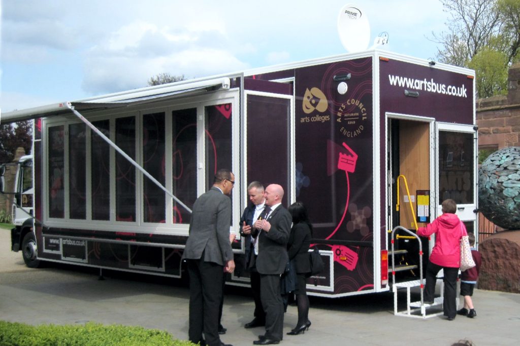 An extension pod on the nearside of a large chassis cab. The pod is fully glazed. Visitors are shown standing in front of the vehicle This is a fine example of what can be achieved with expandable vehicles and trailers